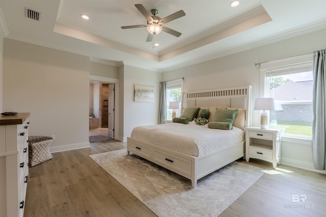 bedroom featuring visible vents, a tray ceiling, multiple windows, and light wood-type flooring