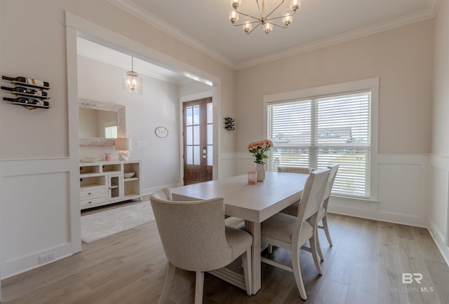 dining space with crown molding, a notable chandelier, a wainscoted wall, and light wood-type flooring