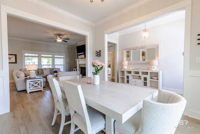 dining space featuring ceiling fan, crown molding, a fireplace, wood finished floors, and baseboards