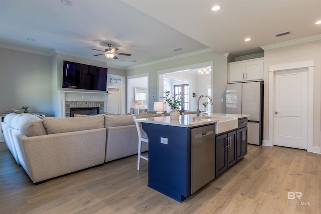 kitchen featuring a sink, light wood-style floors, a kitchen island with sink, a brick fireplace, and stainless steel appliances