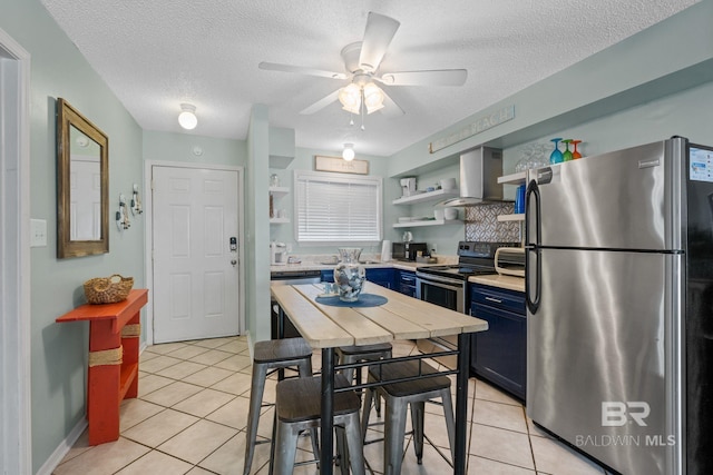 kitchen with light tile patterned floors, stainless steel appliances, blue cabinetry, a textured ceiling, and wall chimney exhaust hood