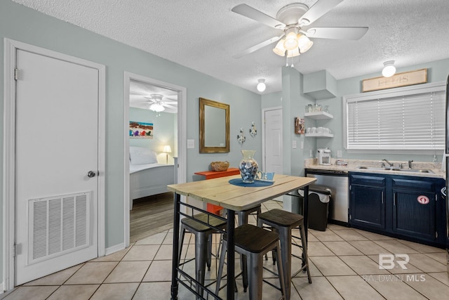 kitchen featuring stainless steel dishwasher, sink, a textured ceiling, light tile patterned floors, and blue cabinets