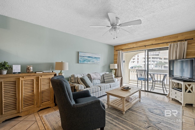 living room with ceiling fan, a textured ceiling, light tile patterned floors, and wooden walls