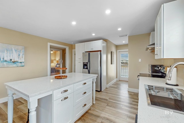 kitchen featuring light hardwood / wood-style flooring, wall chimney exhaust hood, stainless steel refrigerator with ice dispenser, light stone countertops, and white cabinets