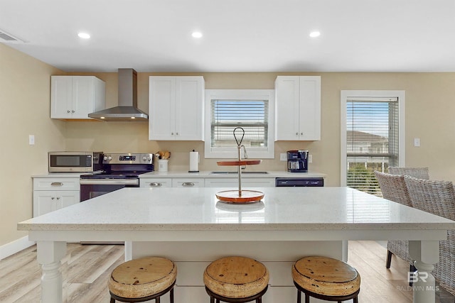 kitchen with wall chimney range hood, light wood-type flooring, white cabinetry, and stainless steel appliances