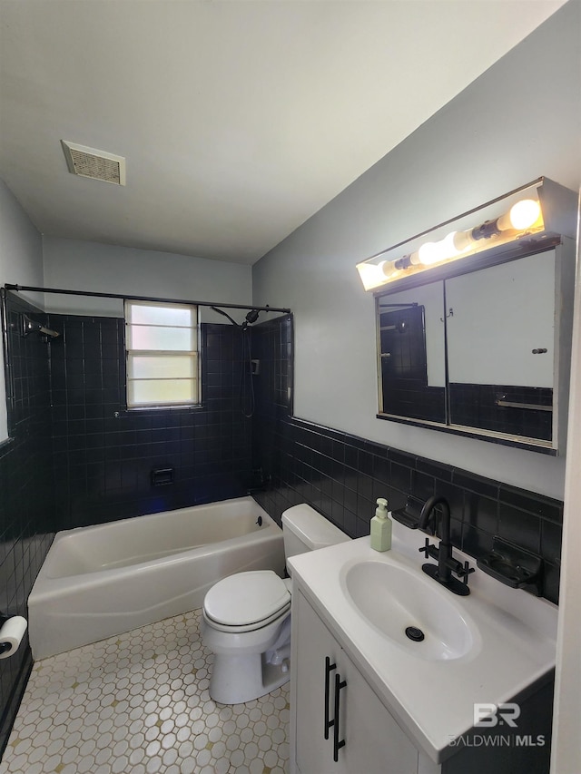 full bathroom with tiled shower / bath, tile floors, tile walls, vanity, and toilet