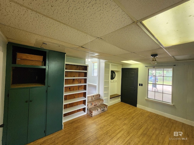 basement featuring light hardwood / wood-style floors, built in shelves, and a drop ceiling