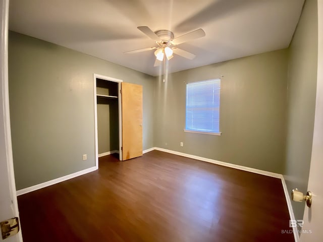 unfurnished bedroom featuring baseboards, dark wood-style flooring, a closet, and ceiling fan