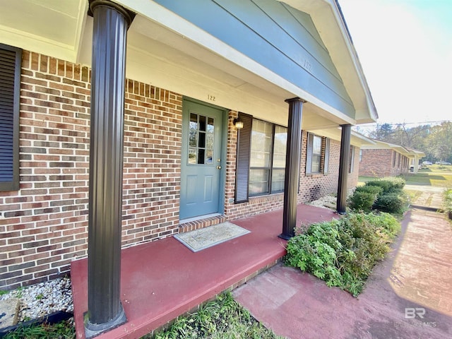 doorway to property with a porch and brick siding