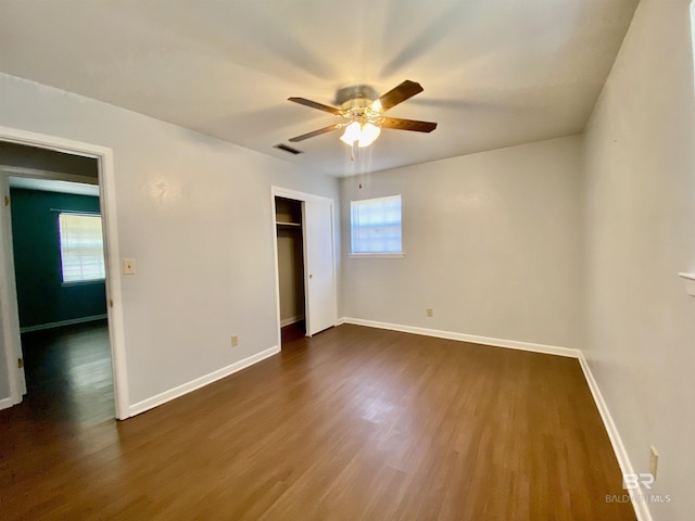 unfurnished bedroom featuring a ceiling fan, a closet, dark wood-type flooring, baseboards, and visible vents