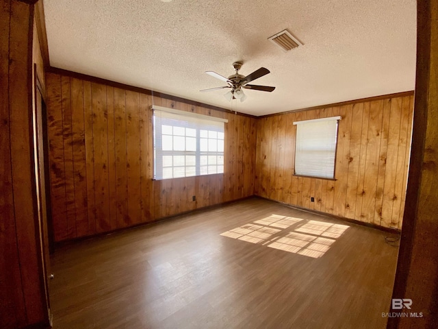 spare room featuring ceiling fan, wood walls, visible vents, and wood finished floors