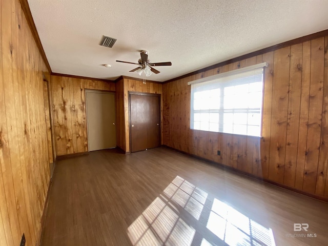 unfurnished bedroom featuring crown molding, wood walls, visible vents, and wood finished floors