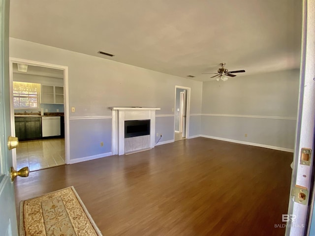unfurnished living room with wood finished floors, a ceiling fan, a fireplace, visible vents, and baseboards