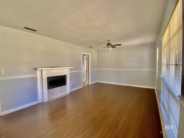 unfurnished living room with wood finished floors, visible vents, a fireplace, a ceiling fan, and baseboards