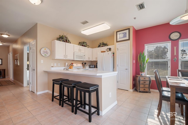 kitchen featuring kitchen peninsula, a breakfast bar, white appliances, light tile patterned floors, and white cabinets