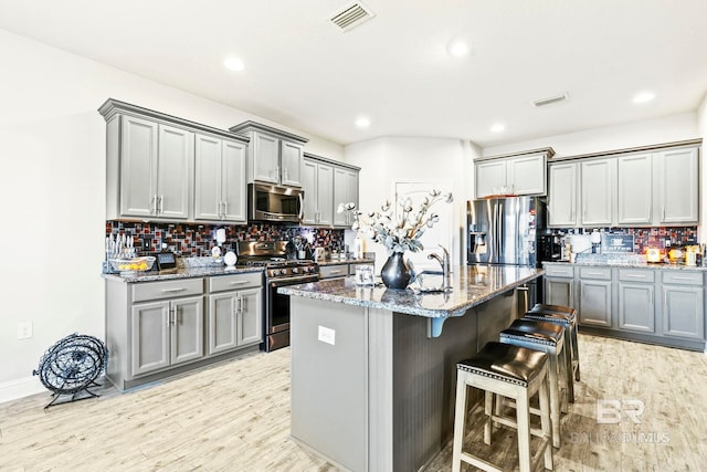 kitchen with backsplash, light hardwood / wood-style flooring, an island with sink, and stainless steel appliances