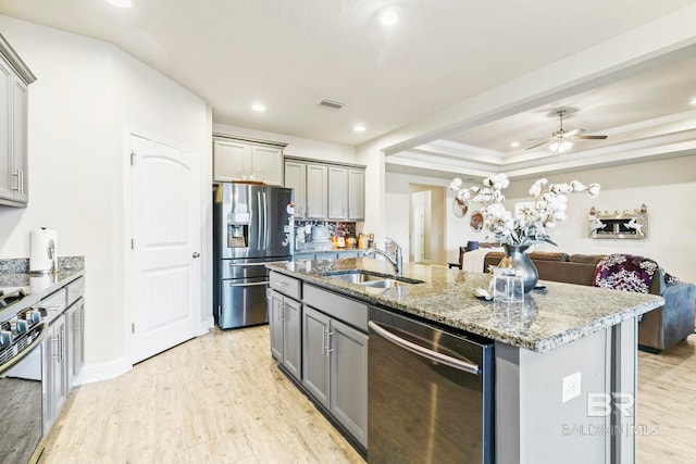 kitchen featuring light wood-type flooring, stainless steel appliances, sink, gray cabinets, and an island with sink