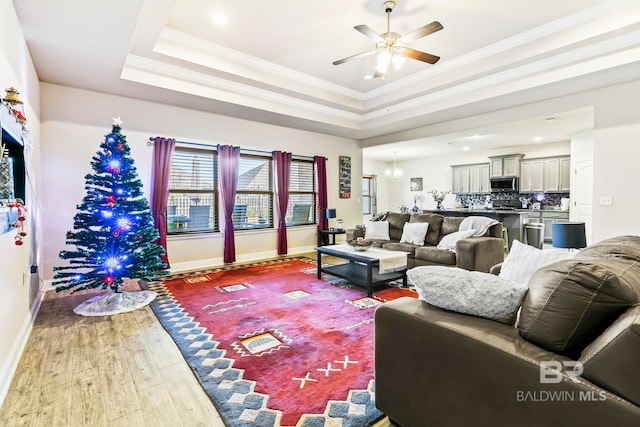 living room featuring wood-type flooring, a raised ceiling, ceiling fan, and crown molding