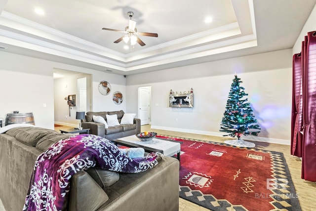 living room featuring a tray ceiling, light hardwood / wood-style flooring, ceiling fan, and ornamental molding