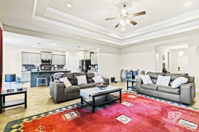 living room with a raised ceiling, ceiling fan, light hardwood / wood-style flooring, and crown molding