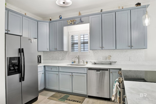 kitchen with appliances with stainless steel finishes, ornamental molding, sink, pendant lighting, and light hardwood / wood-style floors