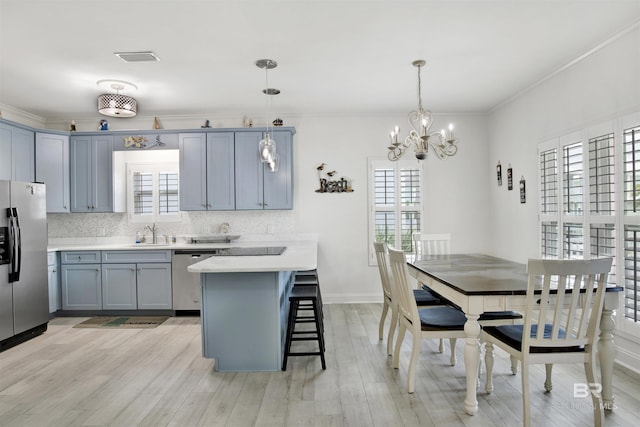 kitchen featuring light wood-type flooring, a breakfast bar, stainless steel appliances, decorative light fixtures, and a notable chandelier