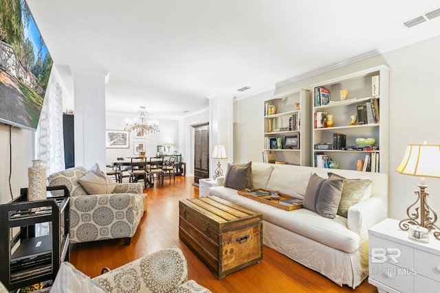 living room with a notable chandelier, wood-type flooring, crown molding, and ornate columns