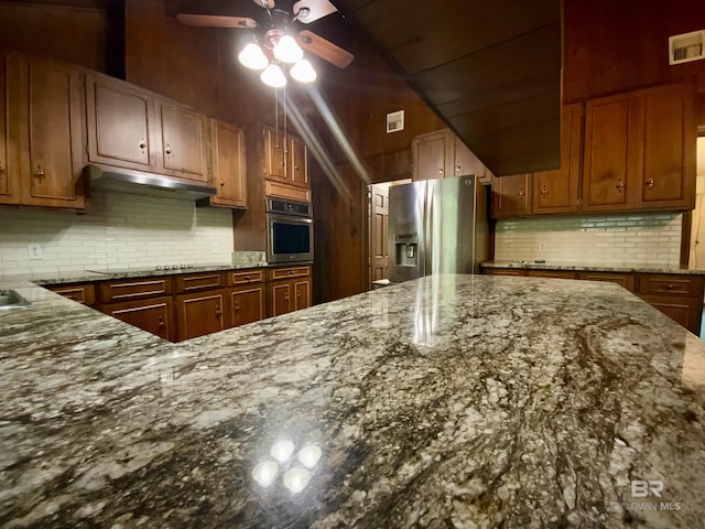 kitchen featuring backsplash, stone counters, ceiling fan, and stainless steel appliances