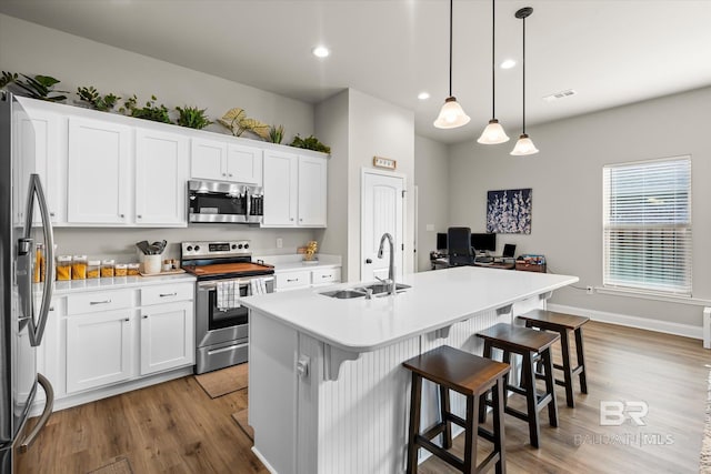 kitchen with sink, decorative light fixtures, white cabinets, a kitchen island with sink, and appliances with stainless steel finishes