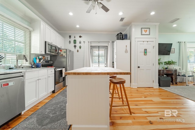 kitchen with a wealth of natural light, white cabinets, appliances with stainless steel finishes, and light wood-type flooring