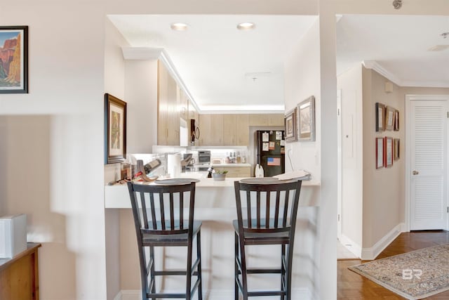 kitchen with kitchen peninsula, wood-type flooring, black refrigerator, light brown cabinetry, and a breakfast bar