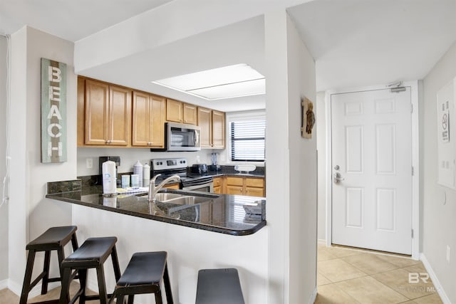 kitchen with a peninsula, a sink, appliances with stainless steel finishes, dark stone countertops, and a kitchen bar