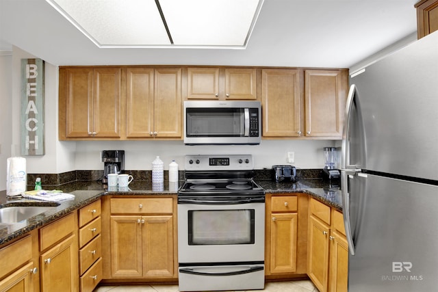 kitchen with dark stone counters, stainless steel appliances, a sink, and light tile patterned flooring