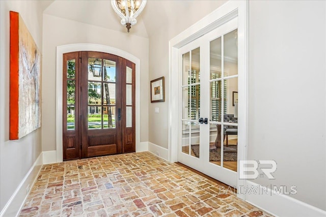 foyer entrance featuring arched walkways, french doors, brick flooring, baseboards, and a chandelier