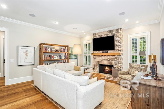 living area with light wood-style flooring, ornamental molding, baseboards, a brick fireplace, and recessed lighting