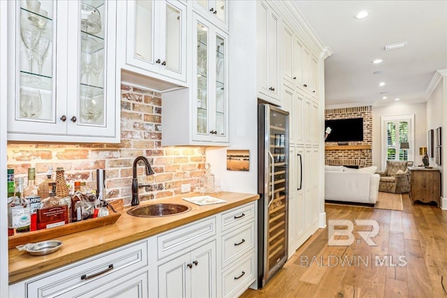 kitchen featuring a sink, wine cooler, wood counters, open floor plan, and ornamental molding