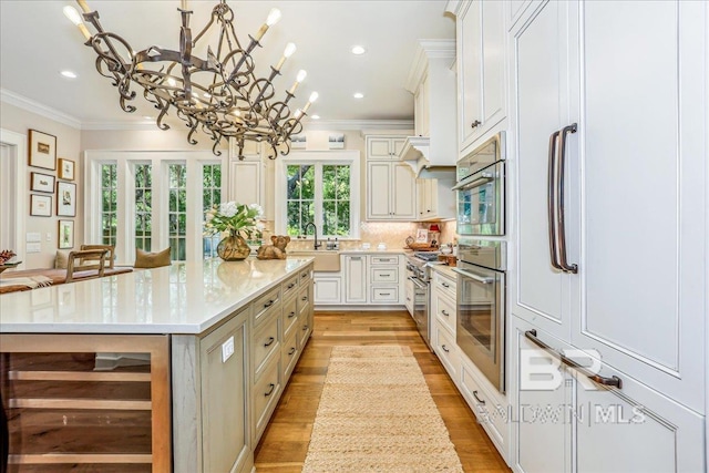 kitchen featuring wine cooler, ornamental molding, a chandelier, a sink, and light wood-type flooring