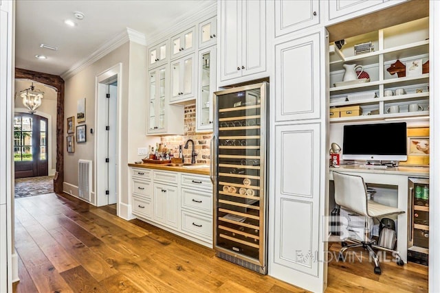 indoor wet bar with beverage cooler, ornamental molding, a chandelier, wood-type flooring, and baseboards