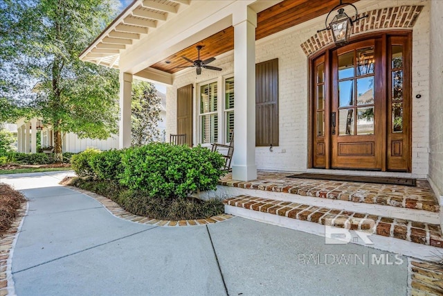 doorway to property featuring a porch, a ceiling fan, and brick siding