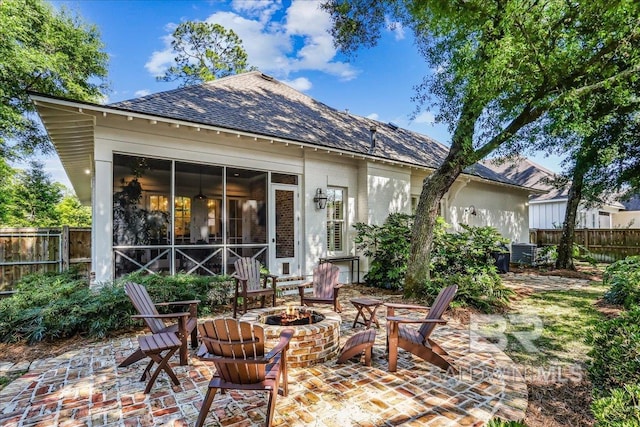 rear view of property featuring a fire pit, a patio, a sunroom, and roof with shingles