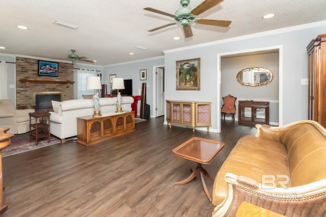 living room featuring ceiling fan, ornamental molding, a textured ceiling, dark hardwood / wood-style floors, and a fireplace