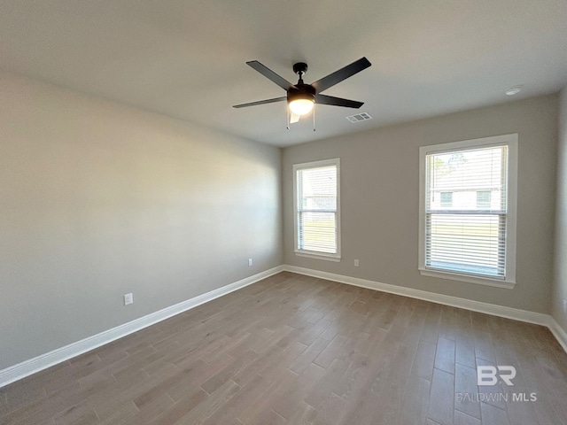 empty room with ceiling fan, visible vents, baseboards, and wood finished floors