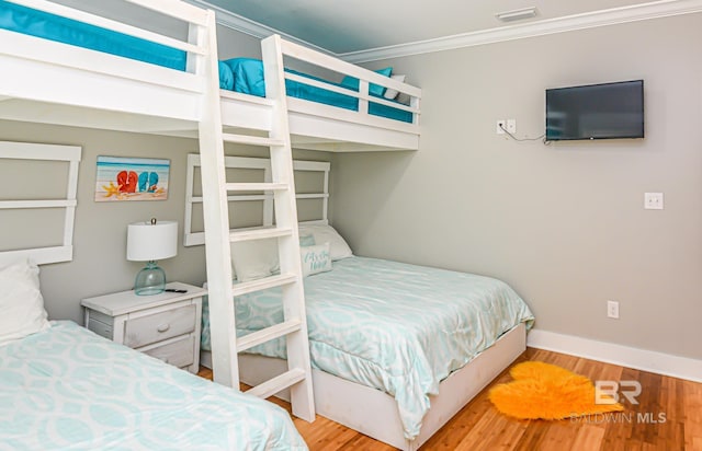 bedroom featuring ornamental molding, wood finished floors, visible vents, and baseboards