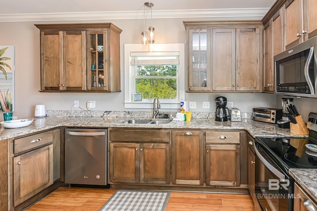 kitchen featuring a sink, appliances with stainless steel finishes, light wood-type flooring, decorative light fixtures, and crown molding