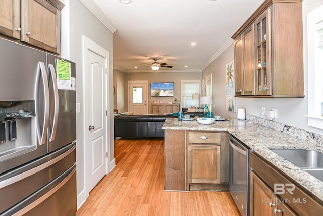 kitchen featuring light wood-style flooring, stainless steel appliances, a peninsula, open floor plan, and ornamental molding