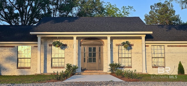 entrance to property with brick siding and a shingled roof