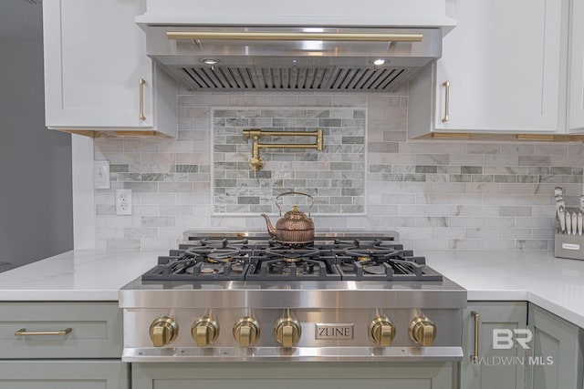 kitchen with ventilation hood, stainless steel gas cooktop, decorative backsplash, light stone counters, and white cabinetry