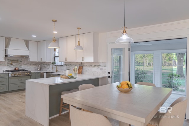 kitchen featuring premium range hood, stainless steel gas cooktop, gray cabinets, tasteful backsplash, and light wood-style floors