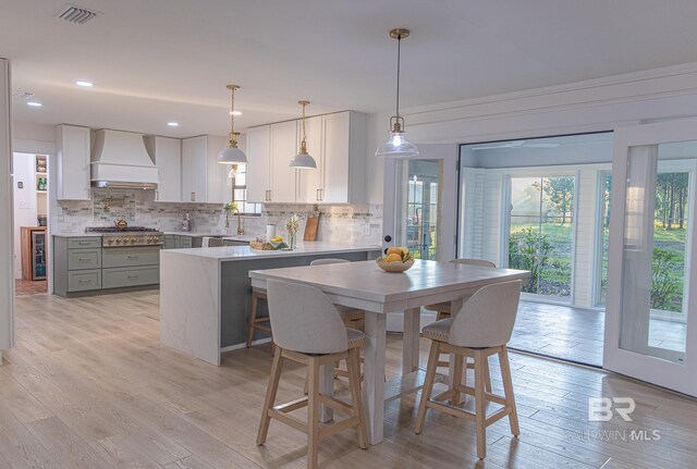 kitchen with custom exhaust hood, decorative backsplash, light countertops, white cabinetry, and a peninsula