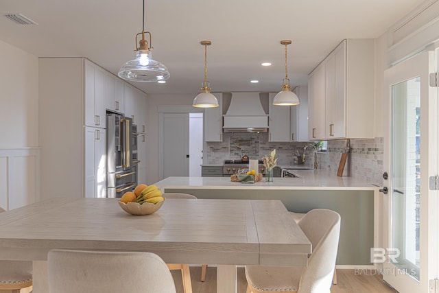 kitchen featuring premium range hood, backsplash, high end refrigerator, light countertops, and recessed lighting